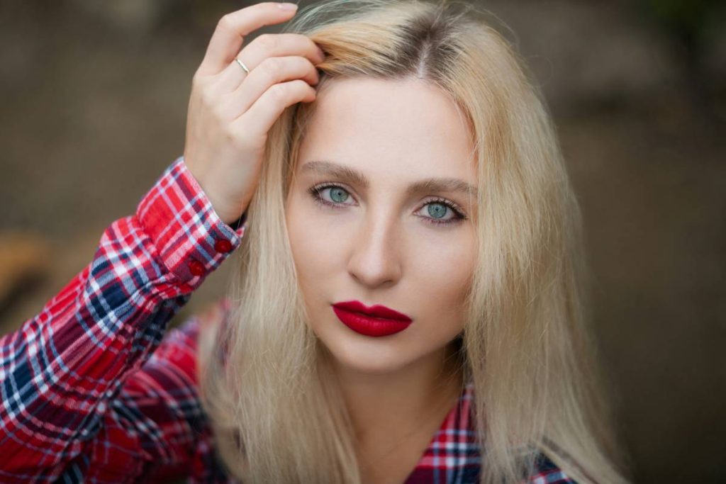 A blonde woman in a red plaid shirt touching her hair